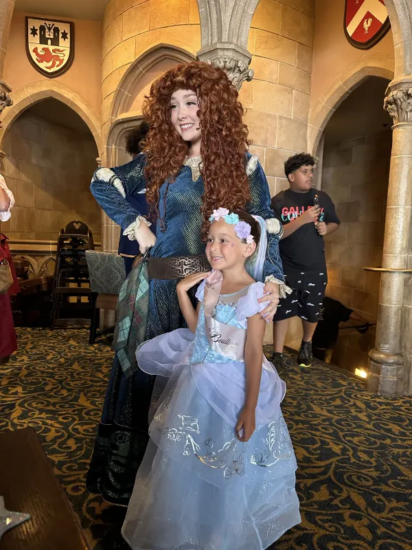 Princess Merida from Brave in the gothic arches of the castle gallery — the princess lineup rotates, so you don't know in advance who you'll meet.