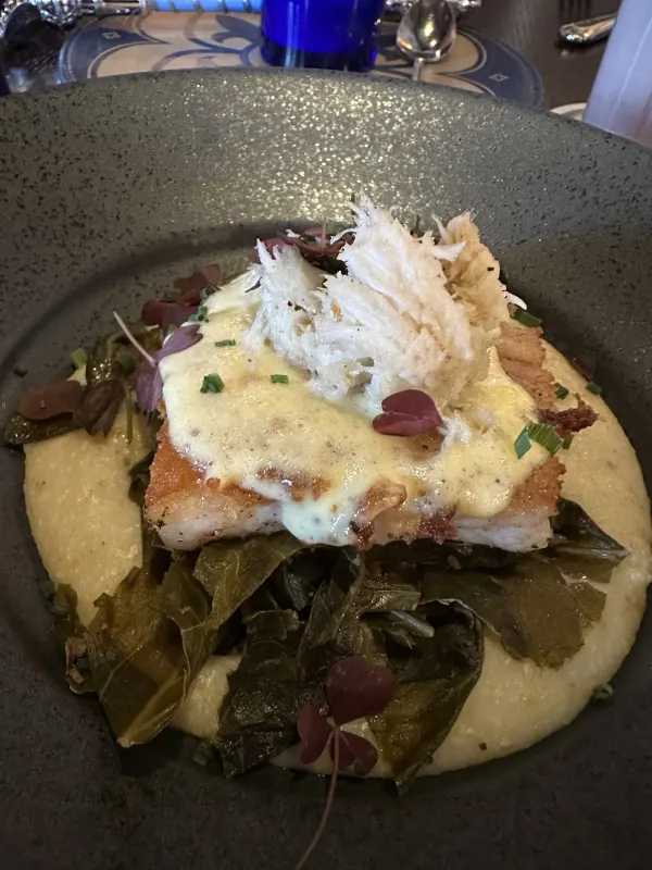 Pan-seared fish with jumbo lump crab, creamy grits, and braised greens — one of the prix fixe entrée options at dinner.
