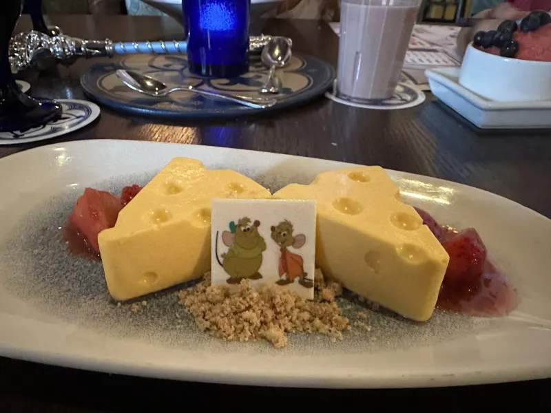'The Clock Strikes Twelve' — the signature lemon-passionfruit dessert plated as a wedge of Swiss cheese with a Jaq-and-Gus card and shortbread 'crumbs.'
