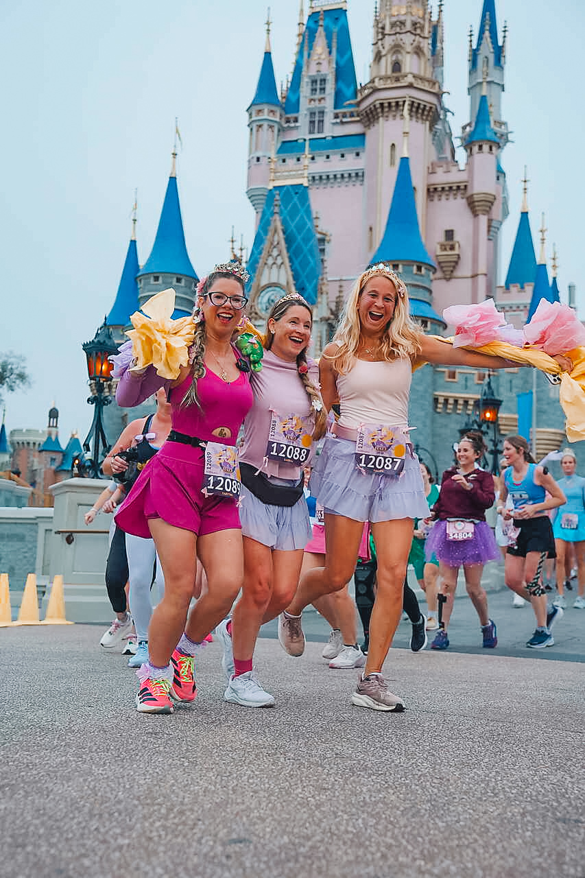 Three runners in princess attire passing Cinderella Castle at runDisney Princess weekend